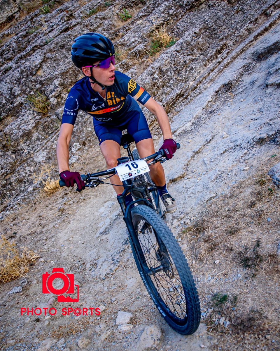 Ana Gay riding down a sloping rock slab with race number 16, looking back over her shoulder